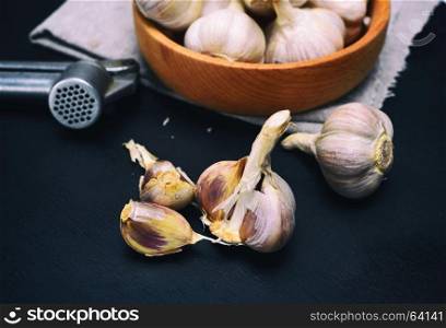Fresh garlic on a black wooden board, next to an iron press for garlic, close up
