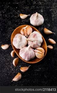 Fresh garlic on a wooden plate. On a black background. High quality photo. Fresh garlic on a wooden plate.