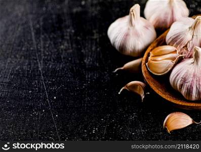 Fresh garlic on a wooden plate. On a black background. High quality photo. Fresh garlic on a wooden plate.
