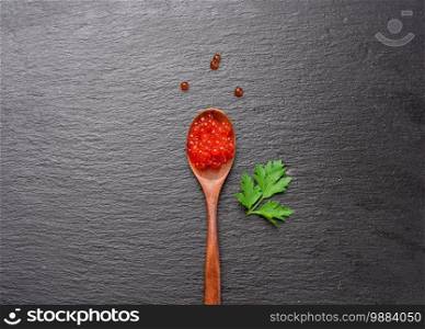 fresh grained red chum salmon caviar in wooden spoon, black background, top view