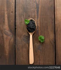 fresh grainy black paddlefish caviar in brown wooden spoon on a black background, top view