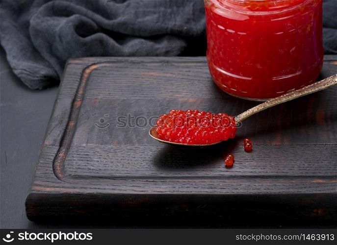 fresh grainy red caviar in a glass jar on a wooden table
