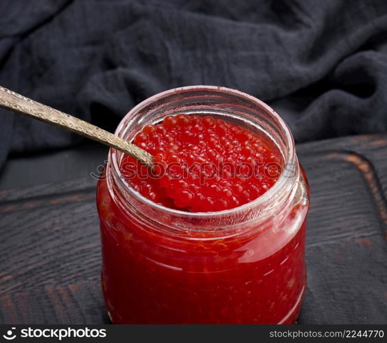 fresh grainy red caviar in a glass jar on a wooden table