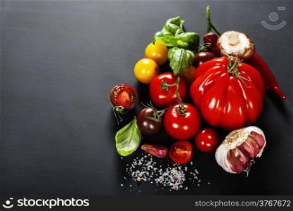 Fresh grape tomatoes with basil and vegetables on a dark background