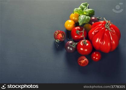 Fresh grape tomatoes with basil and vegetables on a dark background