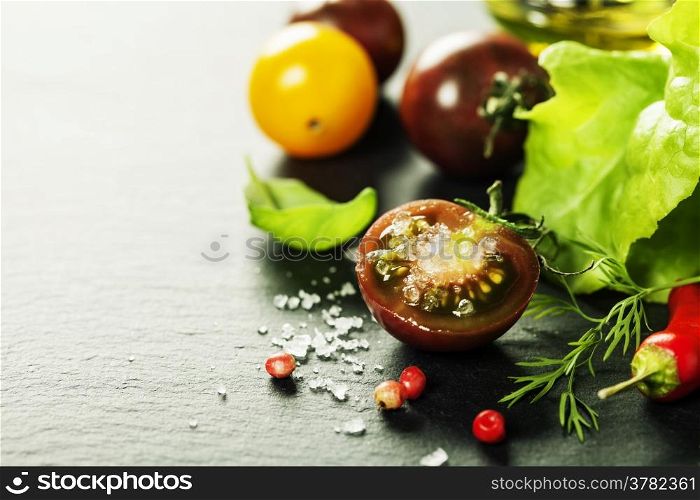 Fresh grape tomatoes with salade leaves and salt for use as cooking ingredients with a halved tomato in the foreground with copyspace