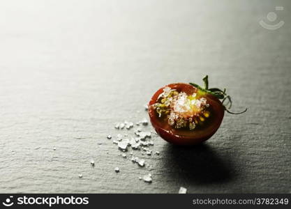 Fresh grape tomatoes with salt for use as cooking ingredients with a halved tomato in the foreground with copyspace