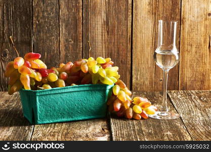 Fresh grapes and glass of grappa on old wooden table