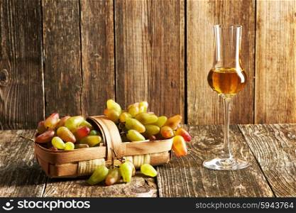 Fresh grapes and glass of grappa on old wooden table