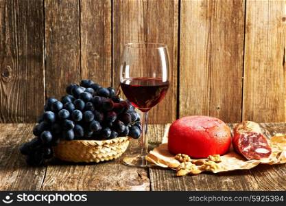 Fresh grapes, cheese and red wine on old wooden table