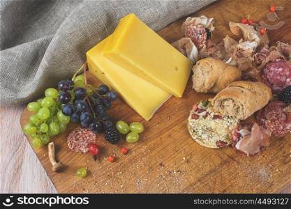 Fresh grapes, cheese bacon berries and salami on wooden table