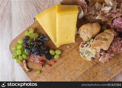 Fresh grapes, cheese bacon berries and salami on wooden table