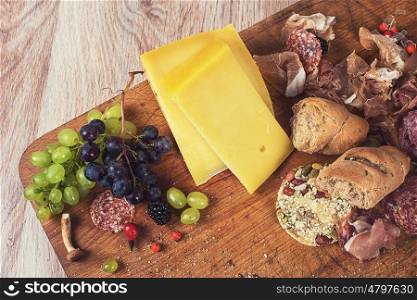 Fresh grapes, cheese bacon berries and salami on wooden table. Toned.