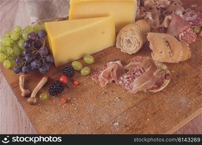 Fresh grapes, cheese bacon berries and salami on wooden table. Toned.