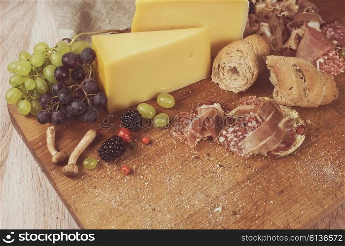 Fresh grapes, cheese bacon berries and salami on wooden table. Toned photo