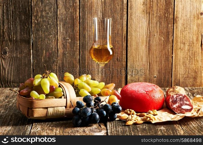 Fresh grapes, grappa and cheese on old wooden table