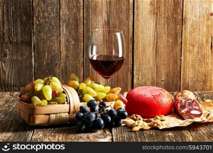 Fresh grapes, red wine and cheese on old wooden table