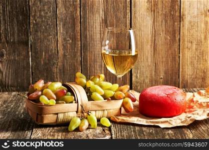 Fresh grapes, white wine and cheese on old wooden table