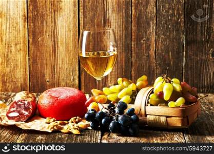 Fresh grapes, white wine and cheese on old wooden table