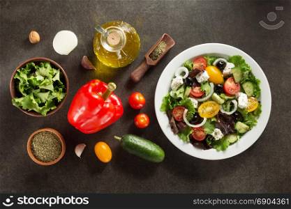 fresh greek salad in plate and ingredients on stone table