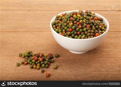 fresh green and orange peppercorns in white ceramic bowl on wood background