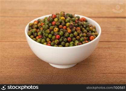 fresh green and orange peppercorns in white ceramic bowl on wood background