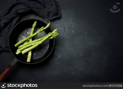 fresh green asparagus in a round cast iron pan on a black table, top view