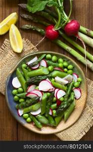 Fresh green asparagus, radish and pea salad served on plate, ingredients on the side, photographed overhead with natural light