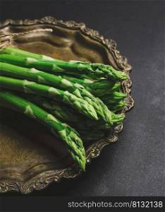 fresh green asparagus sprouts on a round copper plate, black background. View from above
