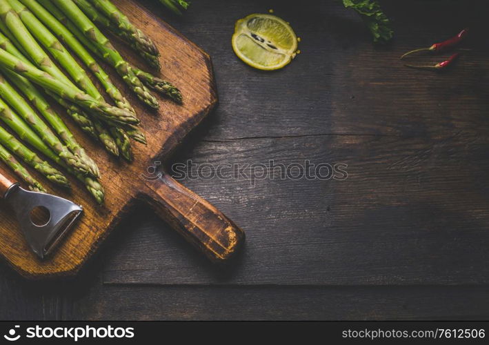 Fresh green asparagus with lemon on vintage wooden cutting board with copper peeler . Vegetarian healthy food. Rustic wooden background. Top view. Place for text.