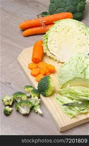 Fresh green broccoli, carrot, garlic, onion and cabbage on a wooden cutting board. Macro photo green fresh vegetable broccoli. Green Vegetables for diet and healthy eating. Organic food preparation.
