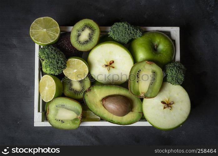 Fresh green fruits and vegetables in a wooden tray on the kitchen table. Above view with healthy food
