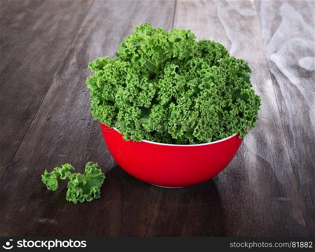 fresh green kale leaves in red ceramic bowl on vintage wooden table