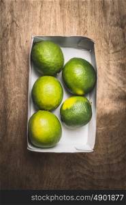 Fresh green lime in paper box on rustic wooden background, top view