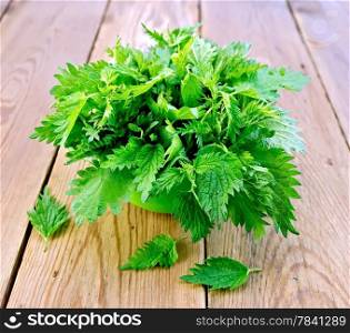 Fresh green nettle in a bowl on a wooden boards background