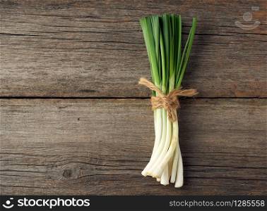 fresh green onion leaves tied with a rope in a bunch on a gray wooden background, top view