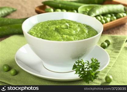 Fresh green pea soup with pea seeds and pea pods around (Selective Focus, Focus on the pea in the middle of the soup). Fresh Green Pea Soup