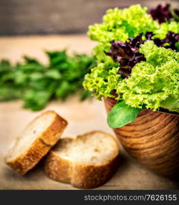 Fresh green salad in the wooden bowl with two piece of tasty bread on the table, organic nutrition, healthy delicious food, vegetarian diet