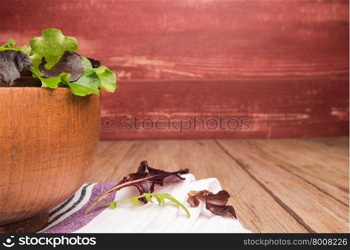 Fresh green salad with spinach, arugula, romaine and lettuce in a bowl on rustic wooden background