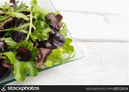 Fresh green salad with spinach, arugula, romaine and lettuce on plate. wood background