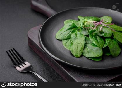 Fresh green spinach leaves on a black ceramic plate on a dark concrete background