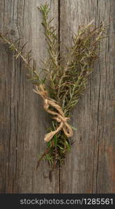 fresh green sprigs of rosemary tied with a brown rope and lie on a gray wooden table from old boards, top view, aromatic spice