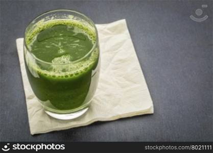 fresh green vegetable juice from cucumber, spinach and cabbage - a glass with napkin on a slate stone background