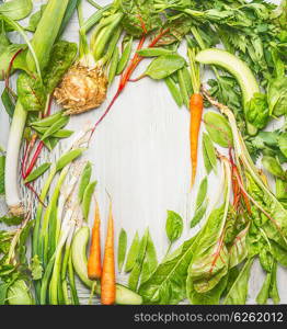 Fresh green vegetables and roots from garden on light wooden background, top view, frame. Vegan and Healthy diet food concept