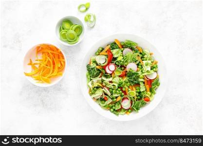 Fresh green vegetarian salad with savoy cabbage, raw carrot, radish, bell pepper, leek and green peas