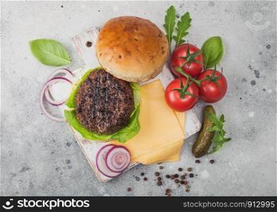 Fresh grilled and raw minced pepper beef burger on vintage chopping board with buns onion and tomatoes on light background. Salty pickles and basil. Top view