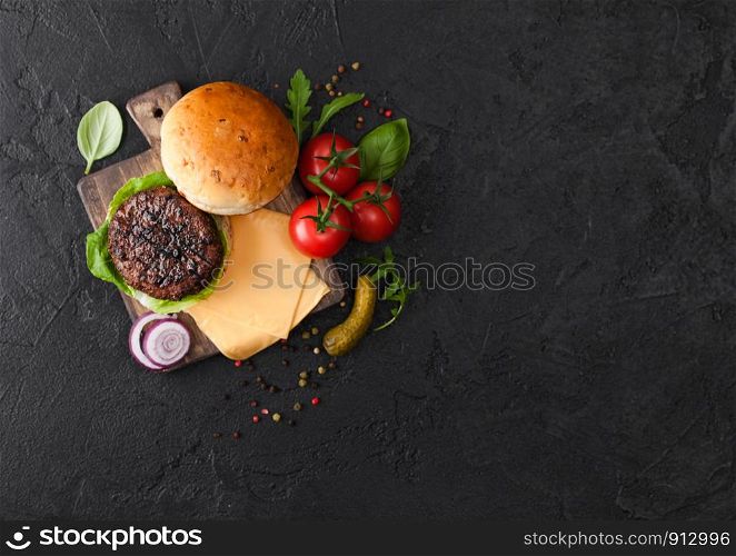 Fresh grilled and raw minced pepper beef burger on vintage chopping board with buns onion and tomatoes on black background. Salty pickles and basil. Top view