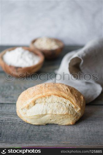 Fresh handicraft bread covered with gray linen napkin lie on the background of old wooden boards. Vertical image with copy-space