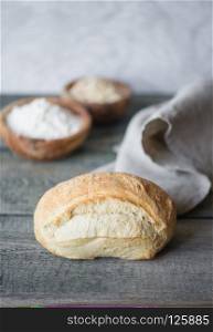 Fresh handicraft bread covered with gray linen napkin lie on the background of old wooden boards. Vertical image with copy-space