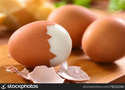Fresh hard boiled eggs with shell beside on wooden board (Selective Focus, Focus on the front of the shell on the first egg)